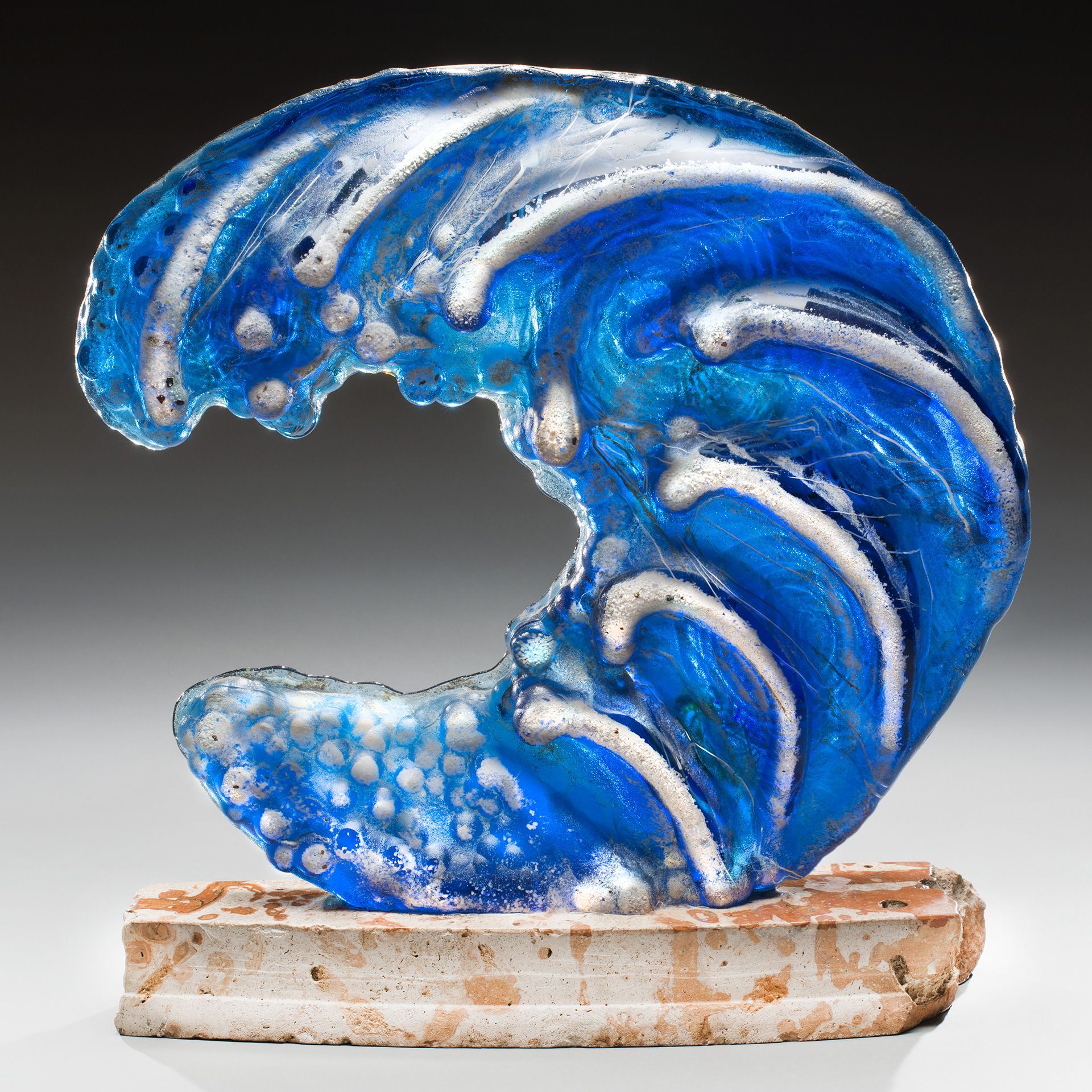 A glass sculpture of a wave on a stone base