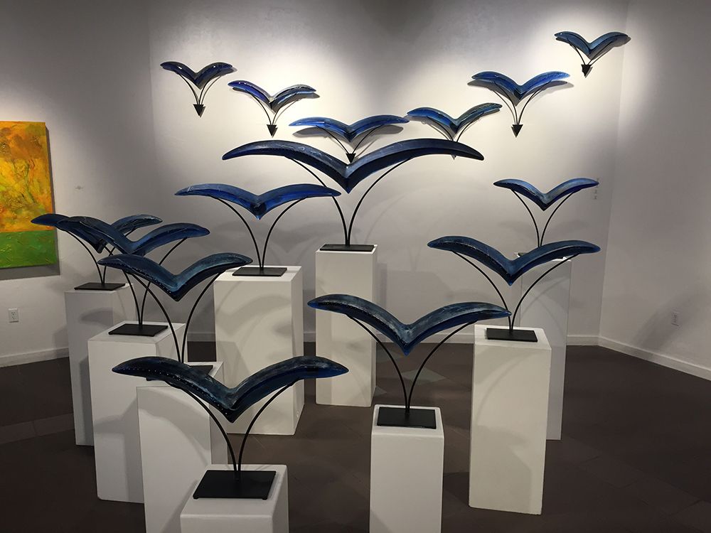 A group of sculptures of birds are sitting on white pedestals in a room.