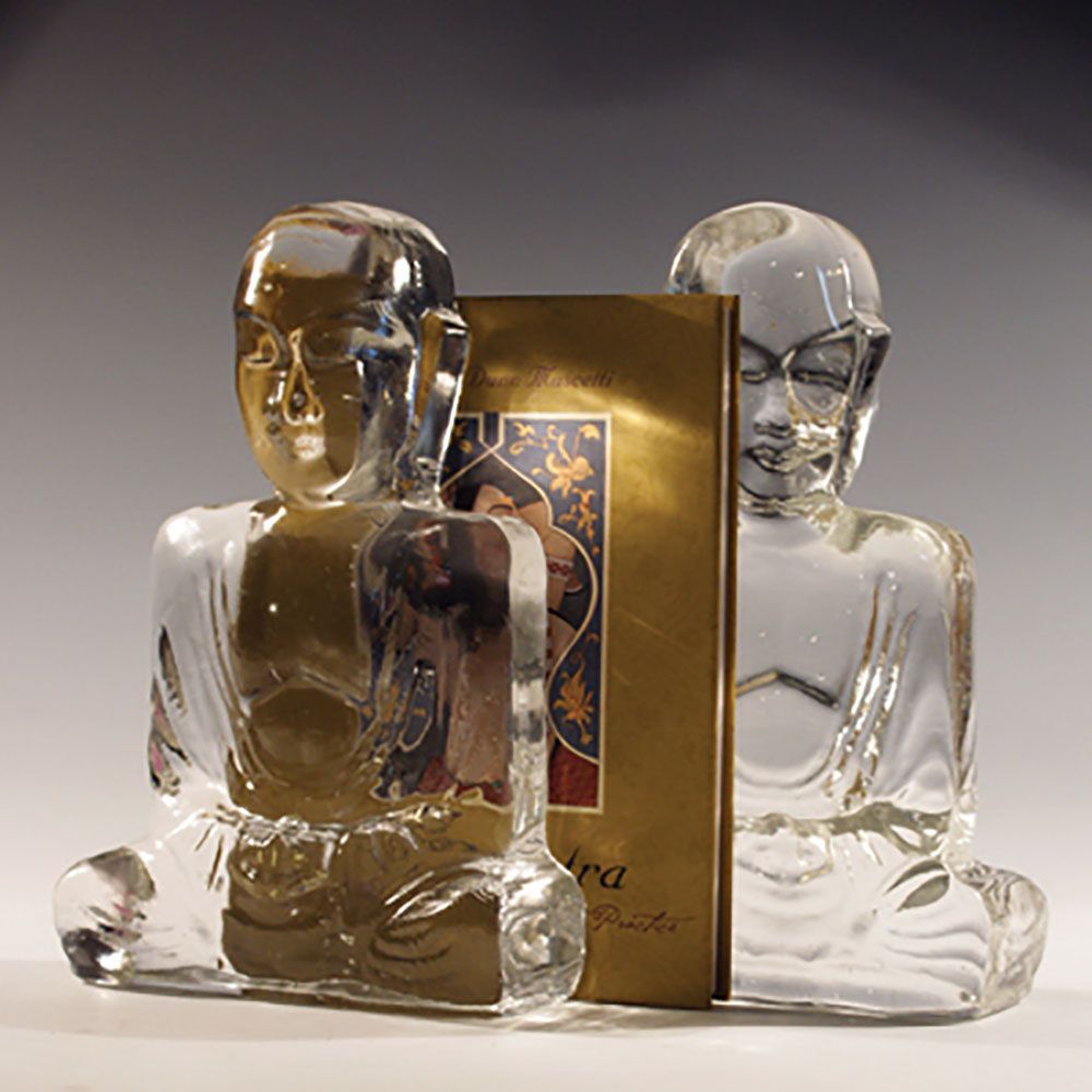Clear glass Buddha bookends with a gold-colored book between them.