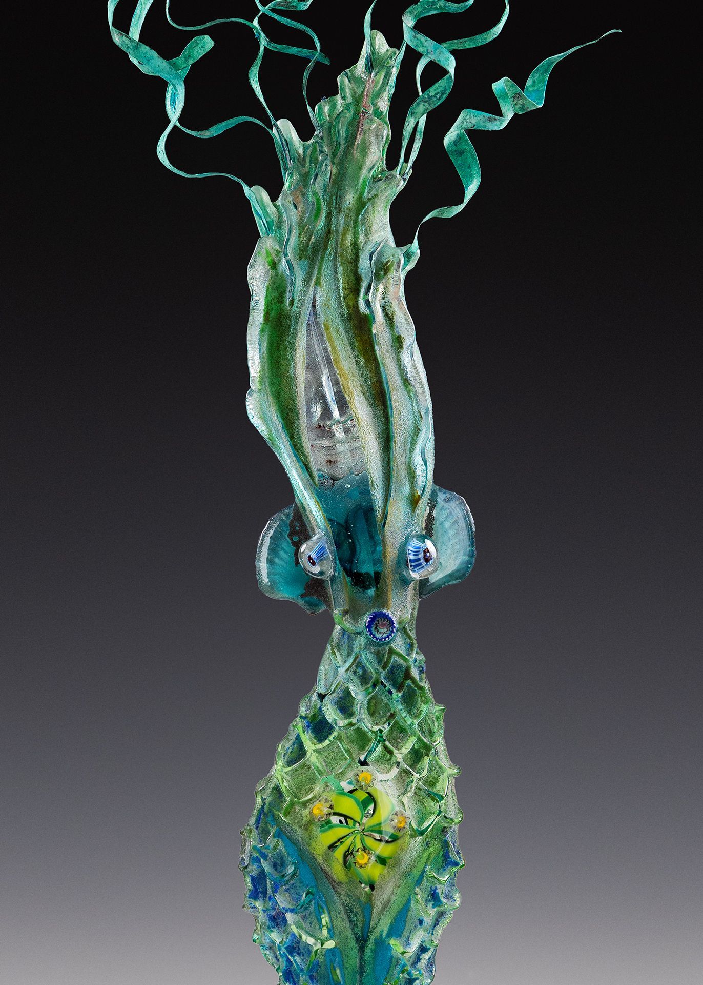 A green and blue sculpture of a squid with ribbons coming out of it 's head