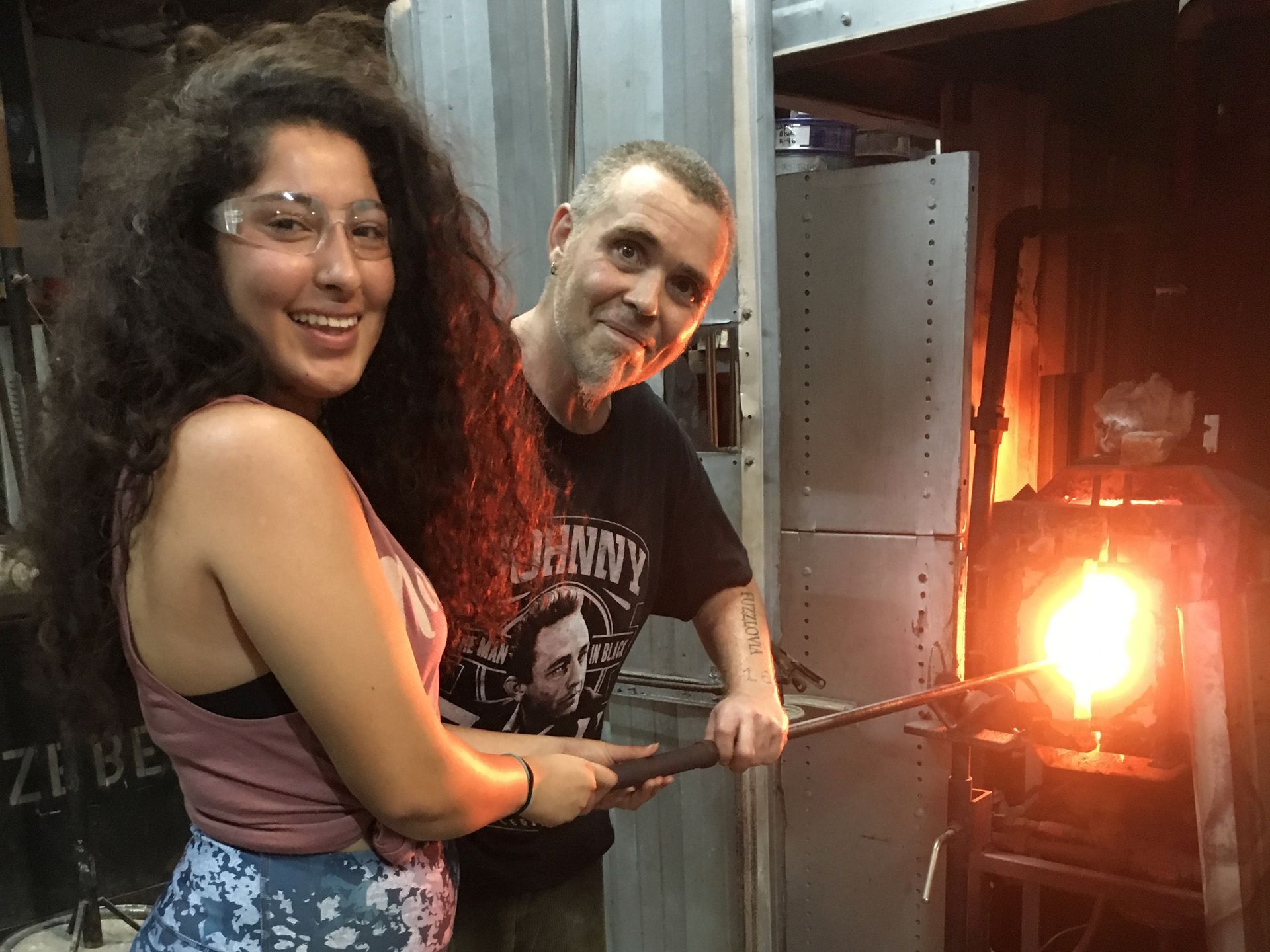 A man and a woman are standing next to each other in front of a glass blowing machine.