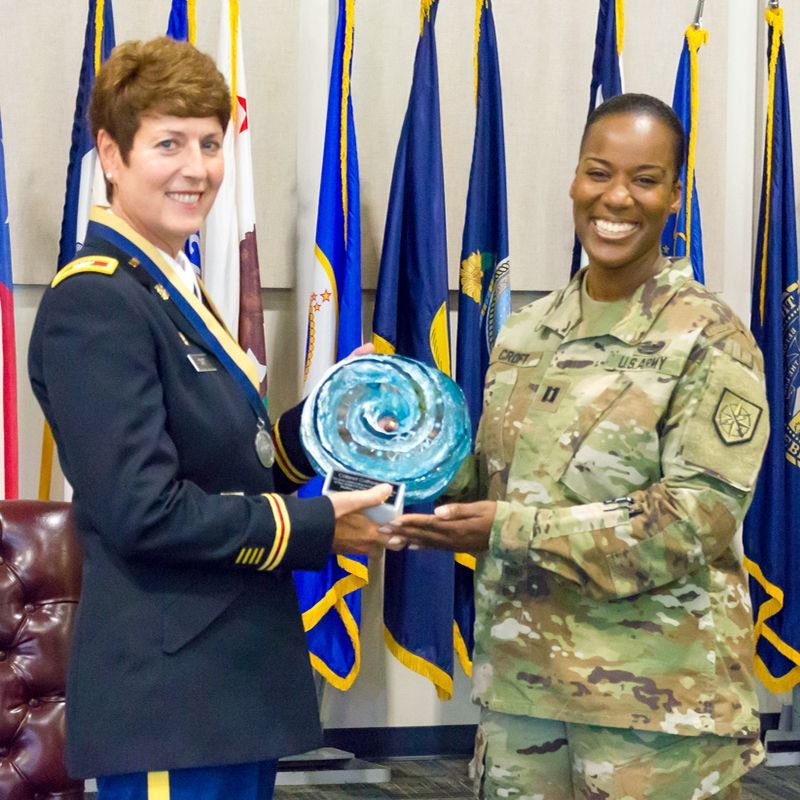 A woman in a military uniform is receiving an award from another woman
