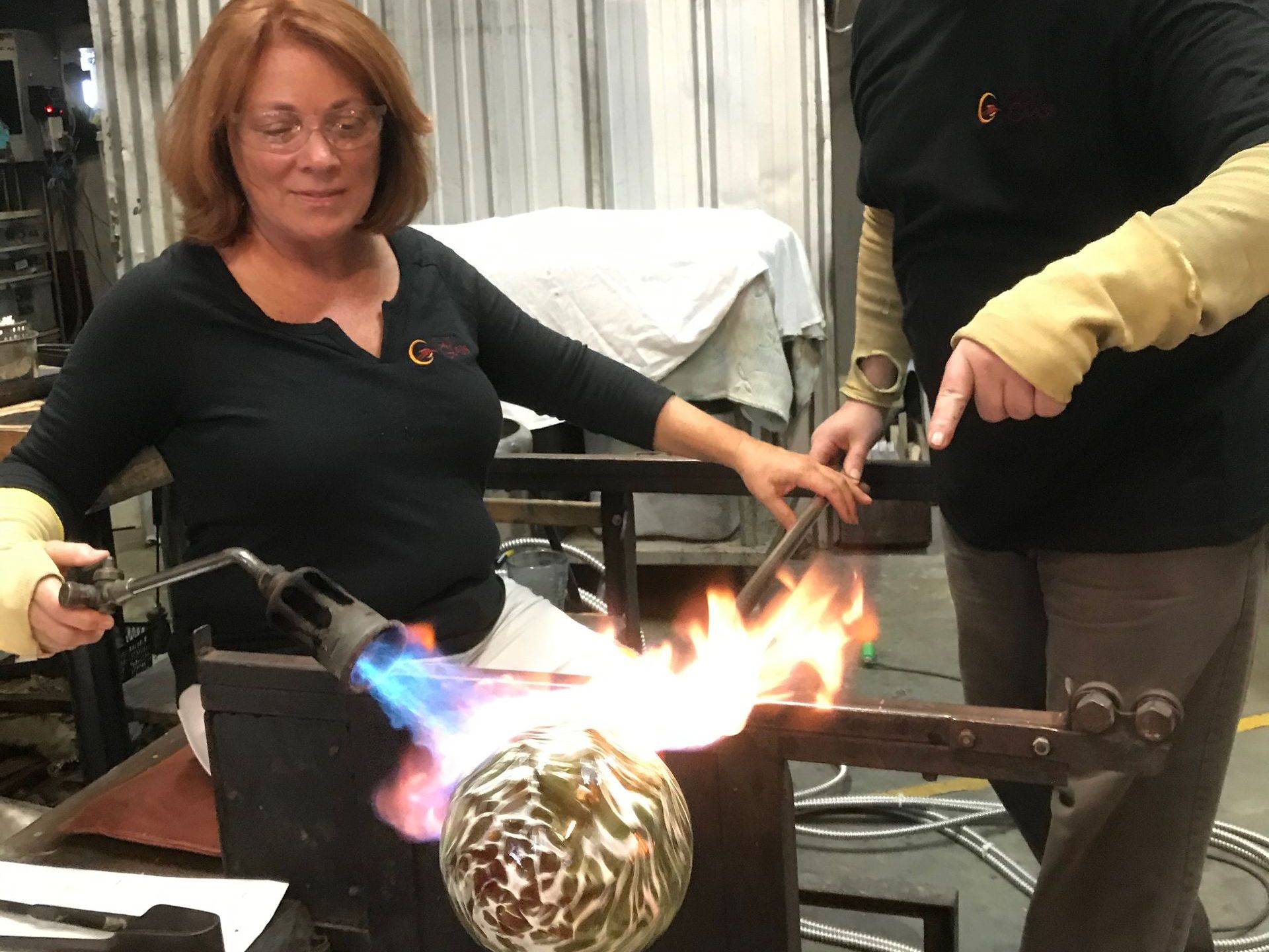 A woman is blowing a glass ball with a torch