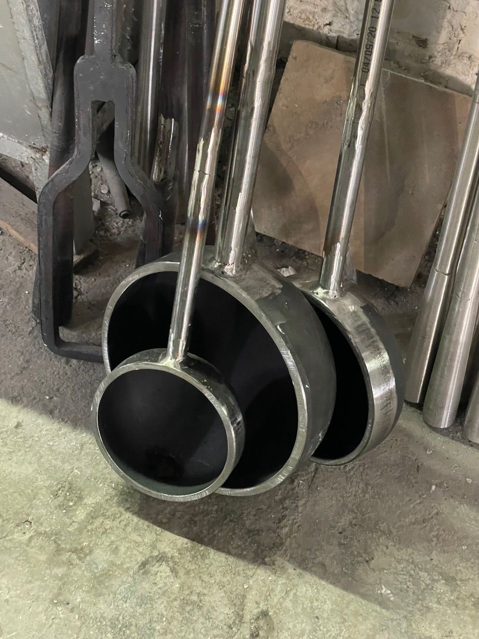 Three metal ladles with long handles resting on a surface, next to other metal tools.