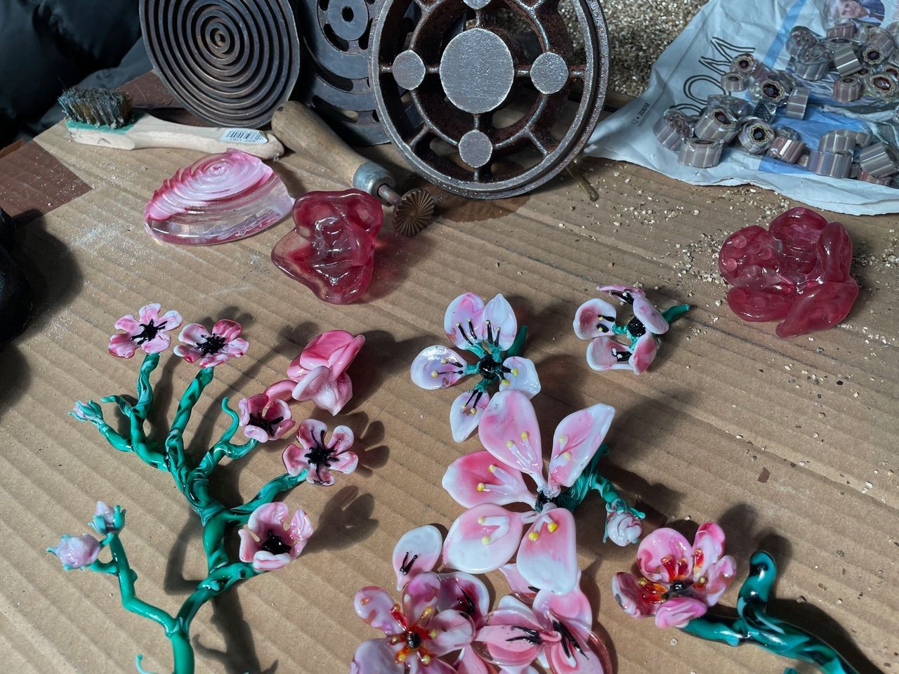 Overhead view of colorful wax flower jewelry components and tools on a wooden surface.