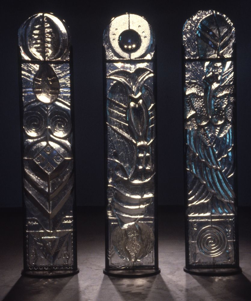 Three stained glass sculptures are lined up in a dark room