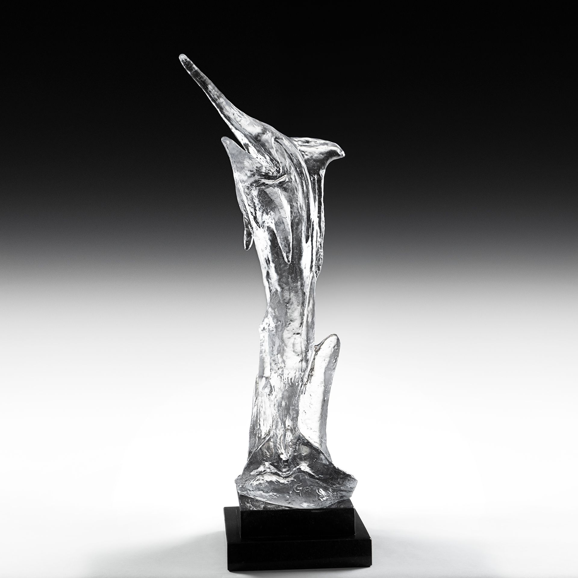A clear glass statue of a dolphin on a black base