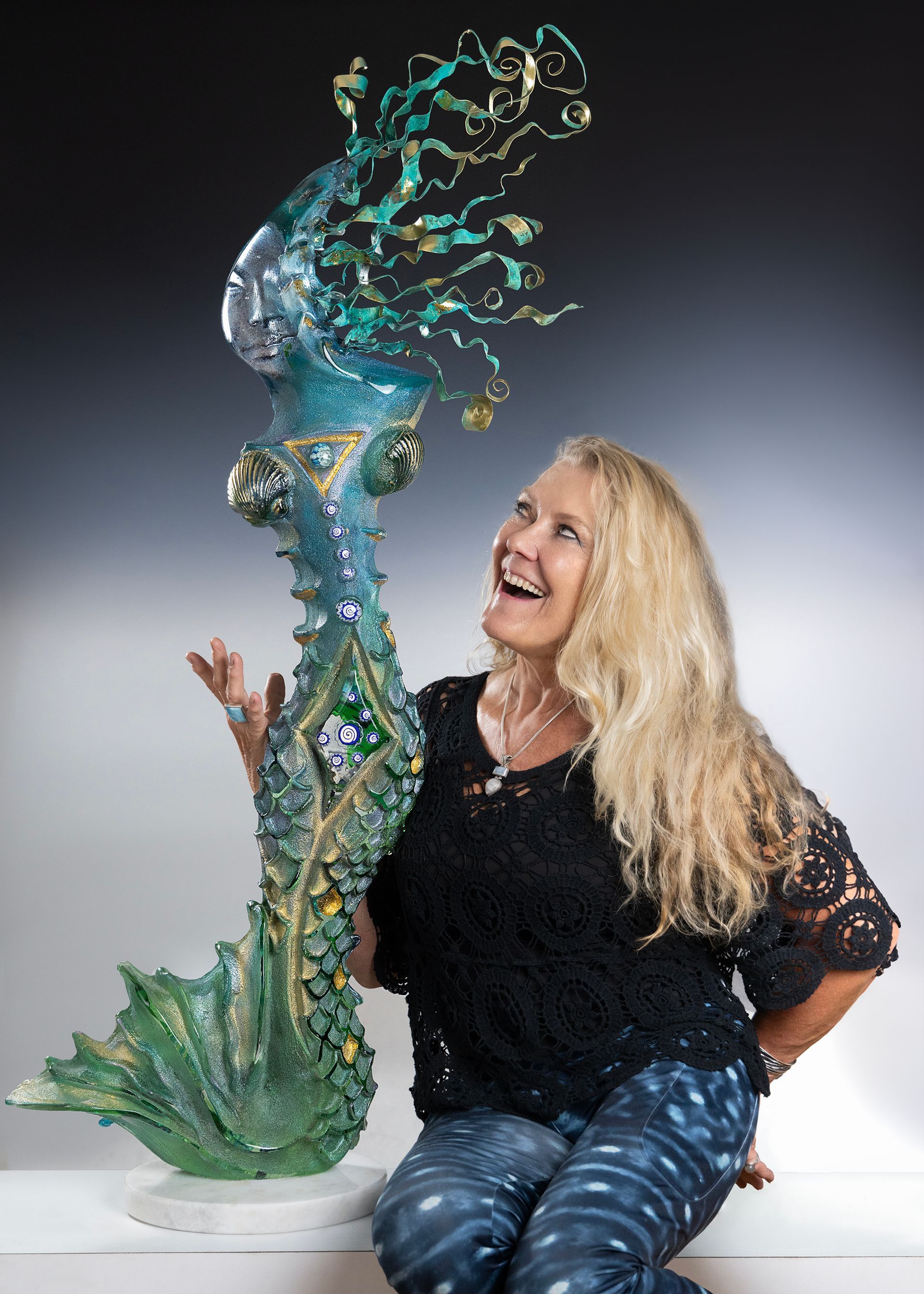 A woman is sitting next to a large sculpture.