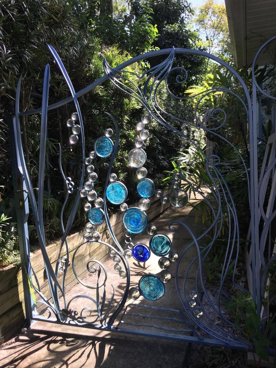 A wrought iron gate with blue beads on it is in a garden.