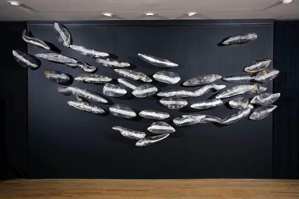 A large sculpture of fish is hanging on a black wall.