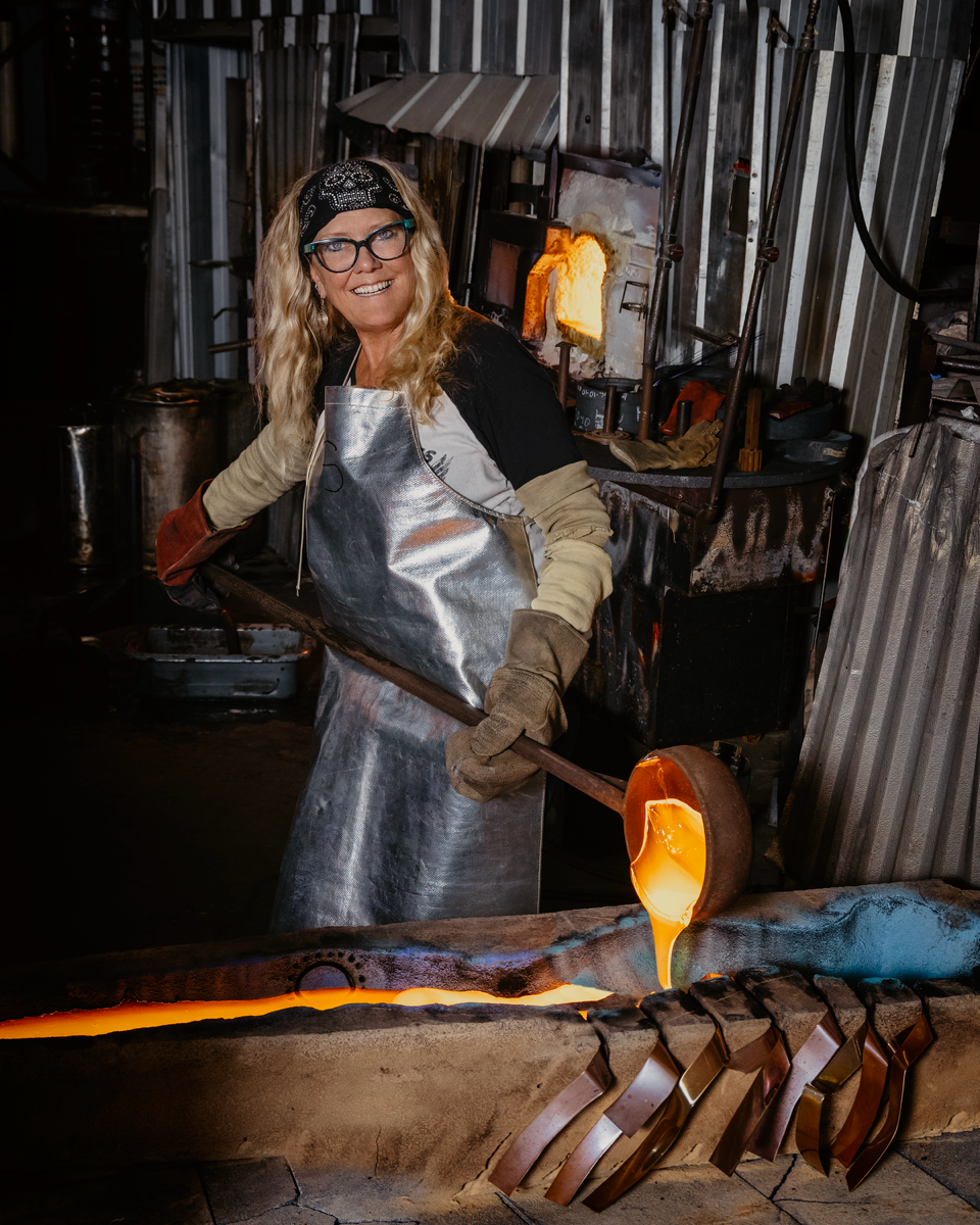 A woman is pouring molten metal into a furnace with a ladle.