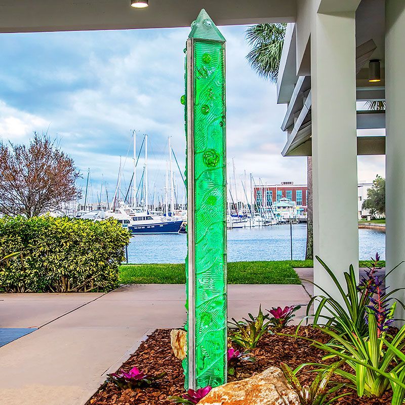 A green sculpture in a garden with boats in the background