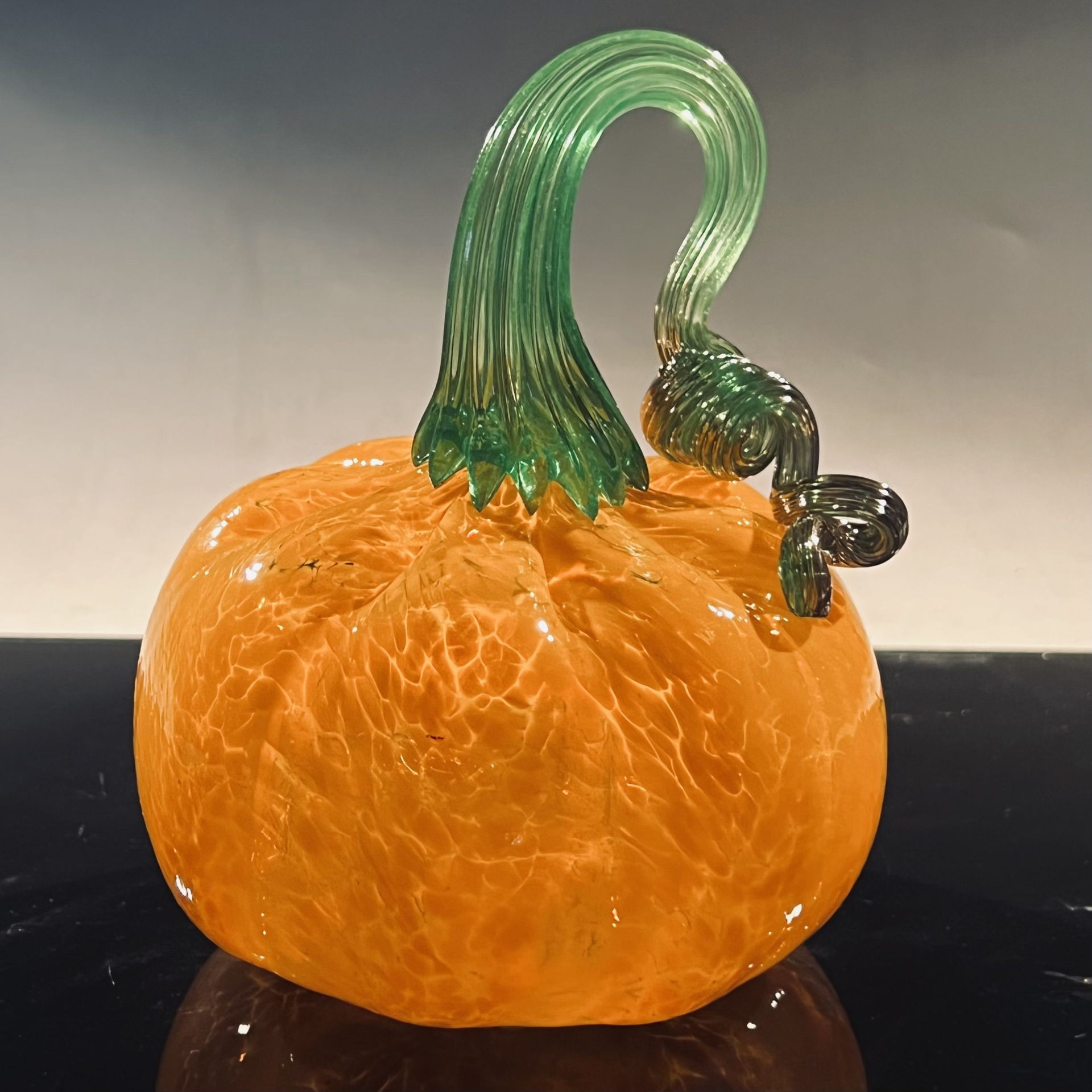 A glass pumpkin with a green stem is sitting on a table