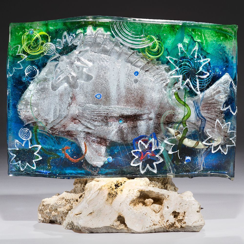 A glass sculpture of a fish on a rock