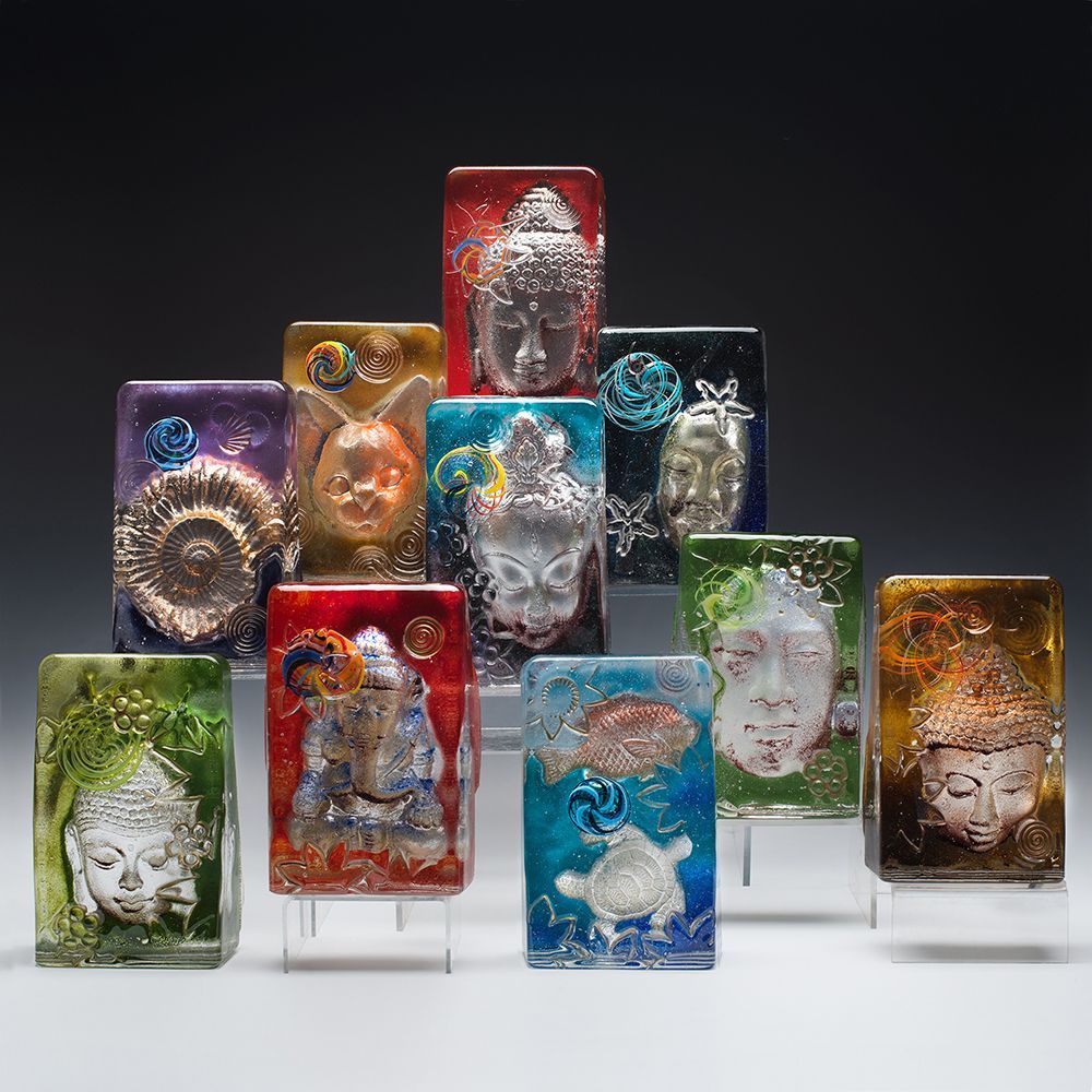 Collection of glass art with various embossed religious figures in rectangular blocks, against a dark backdrop.