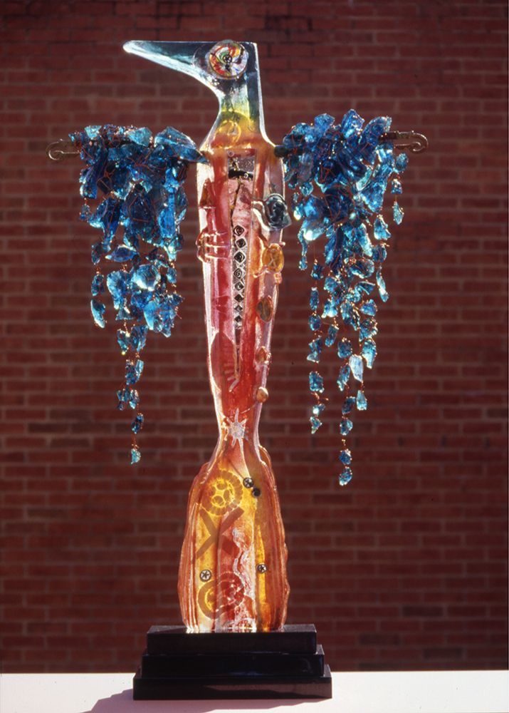A statue of a bird with blue wings is on a table in front of a brick wall