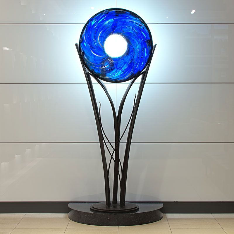 A blue glass sculpture is sitting in front of a wall.