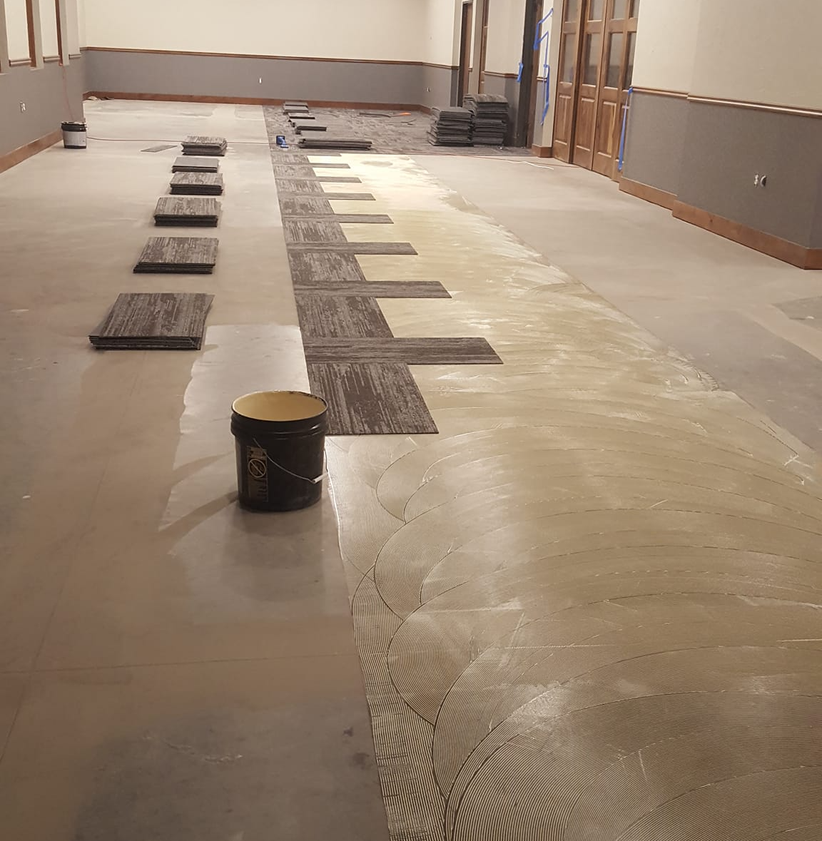 The subfloor is being prepared for this carpet tile installation with the right amount of adhesive applied.