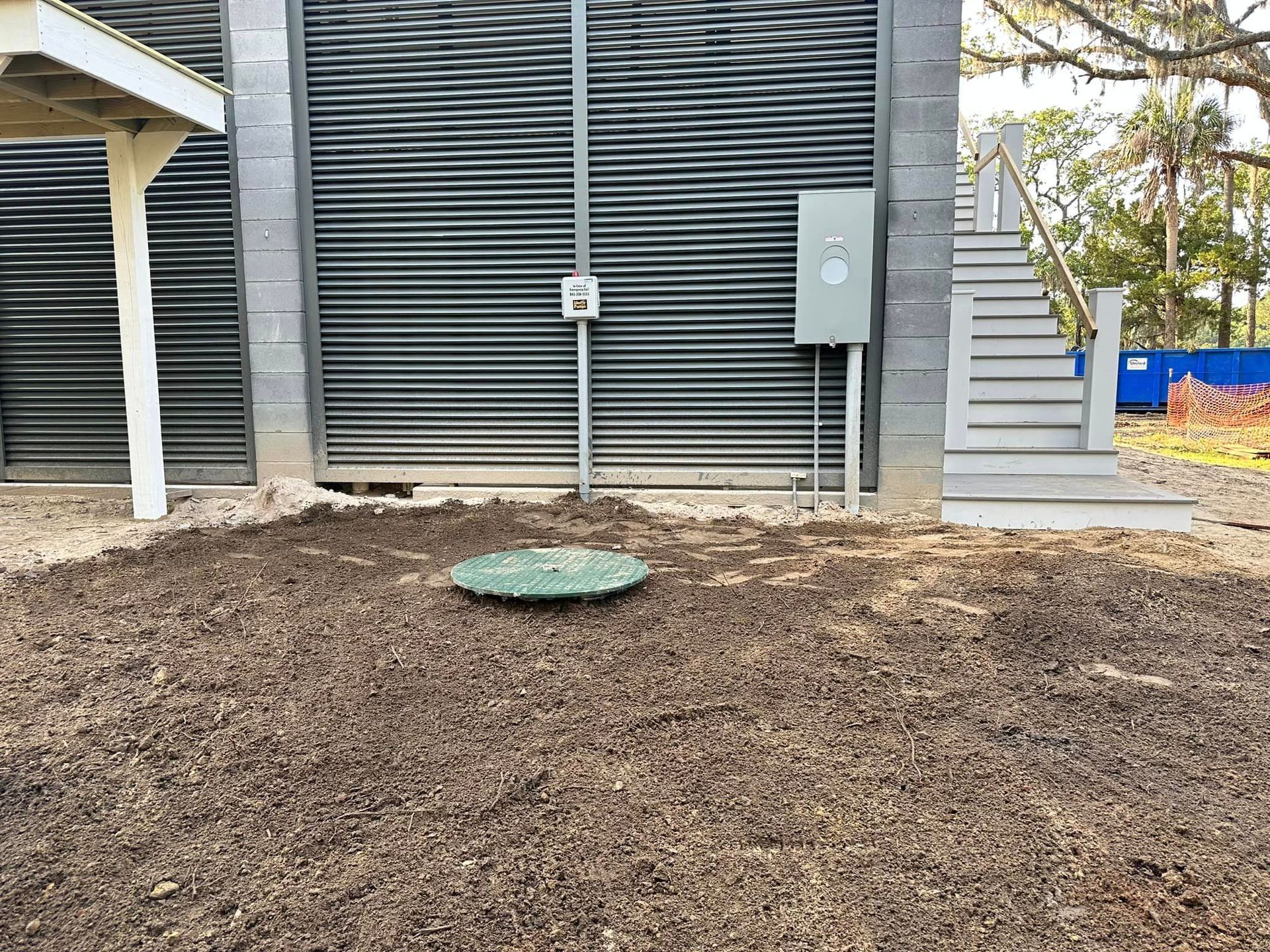 a green septic tank sits in the dirt in front of a building