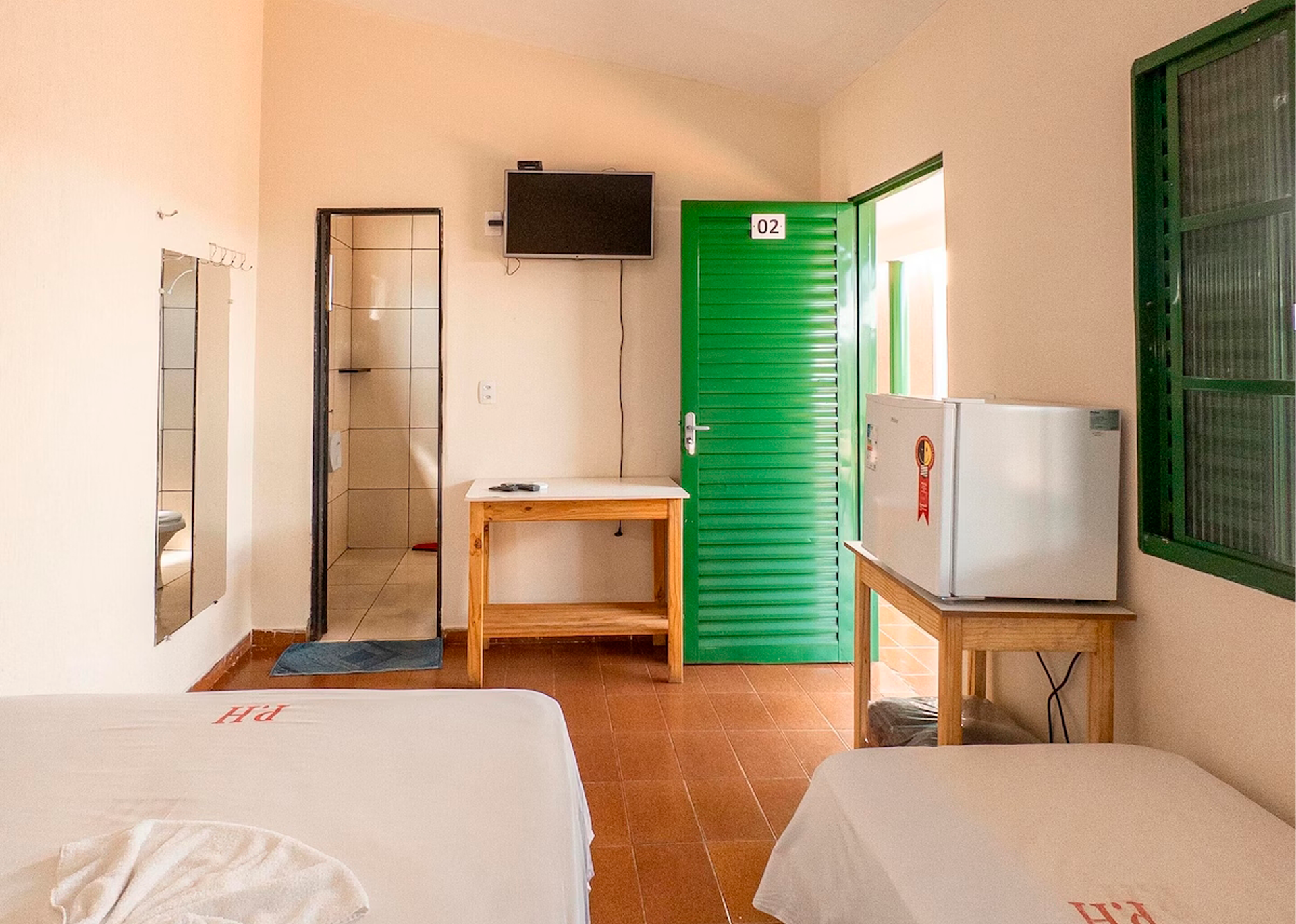 Um quarto de hotel com duas camas, uma geladeira, uma televisão e uma porta verde.