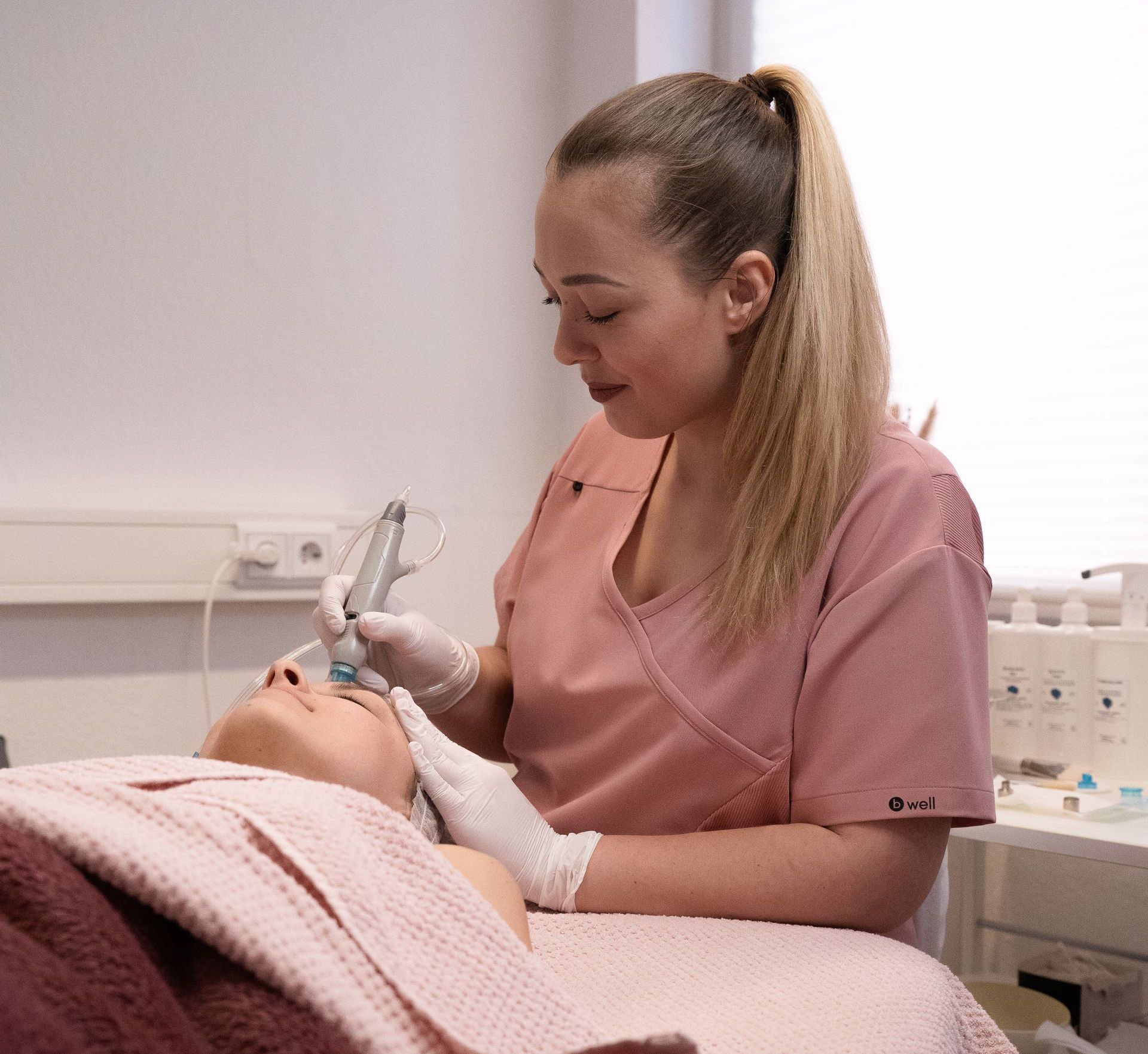 A woman in a pink scrub is working on a patient 's face