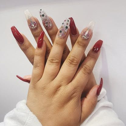 A close up of a woman 's hand with long red nails and rhinestones.