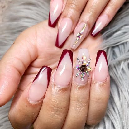 A close up of a woman 's nails with a red french manicure and rhinestones.