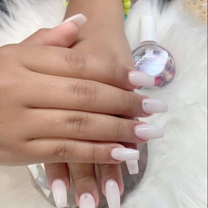 A woman 's hand with long white nails and a bottle of nail polish.