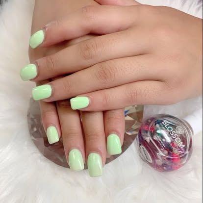 A woman 's hands with green nails and a bottle of nail polish.