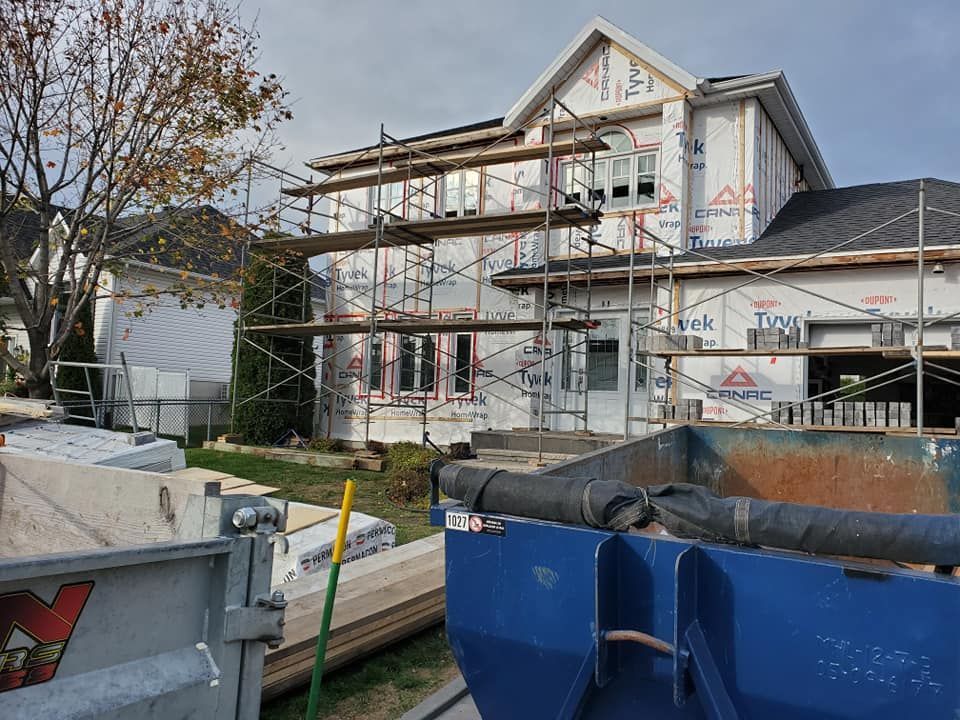 Une maison est en construction avec un échafaudage et une benne à ordures devant.