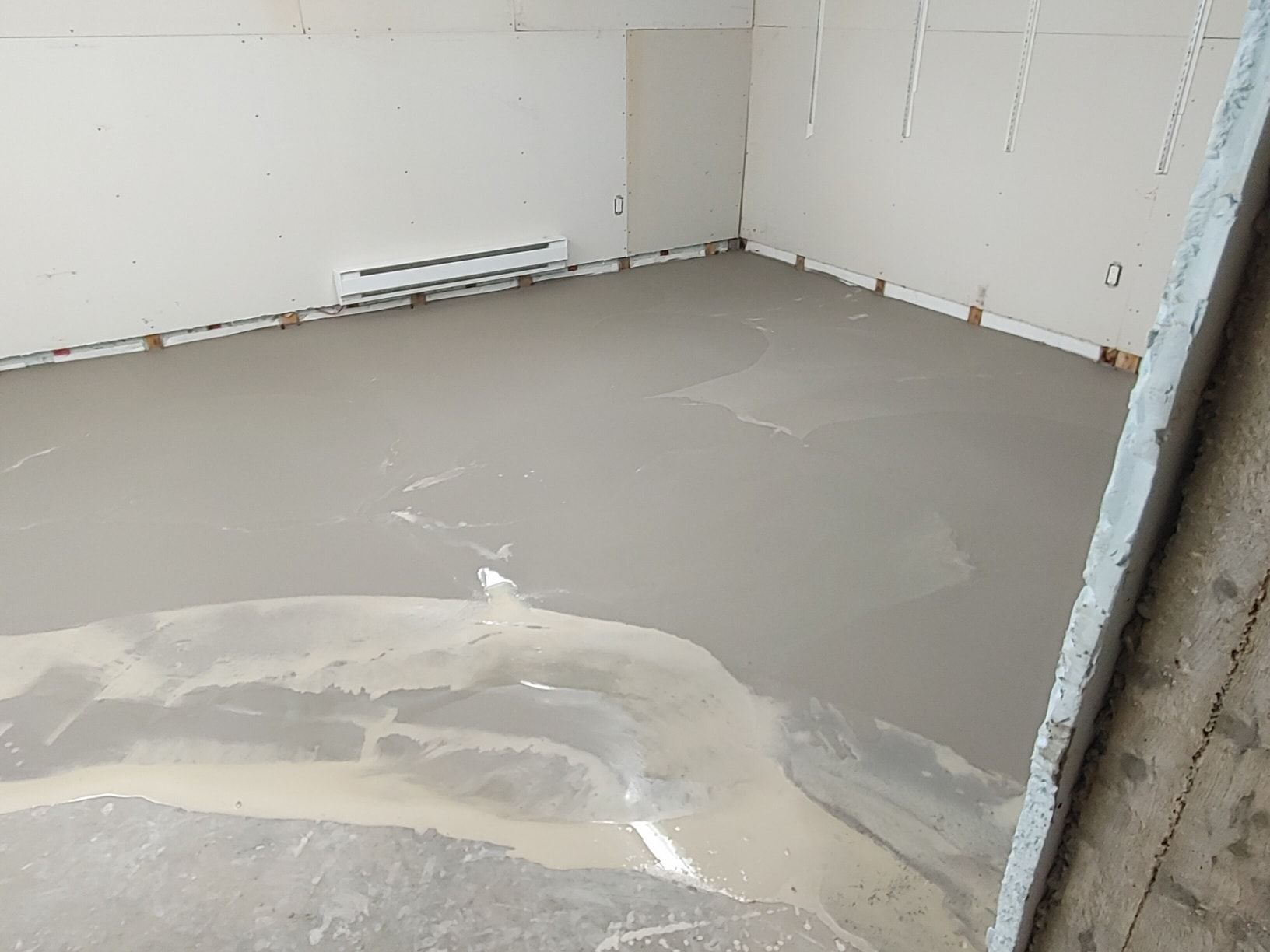 Une pièce avec un sol en béton et des murs blancs.
