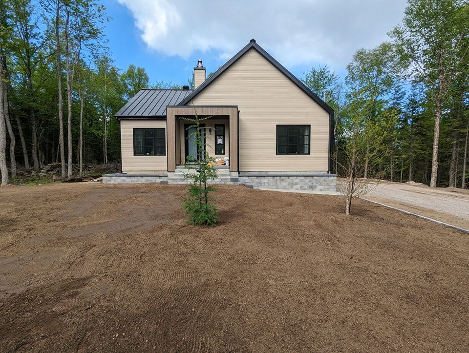 Une petite maison est située au sommet d'un champ de terre au milieu d'une forêt.