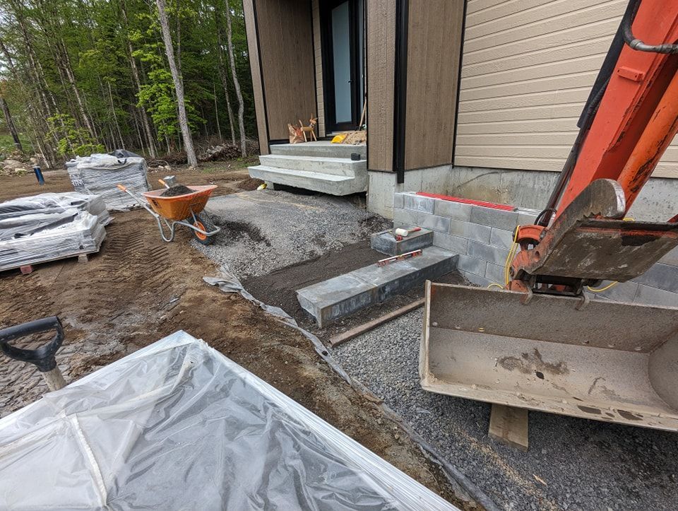 Une excavatrice creuse un trou dans le sol devant une maison.