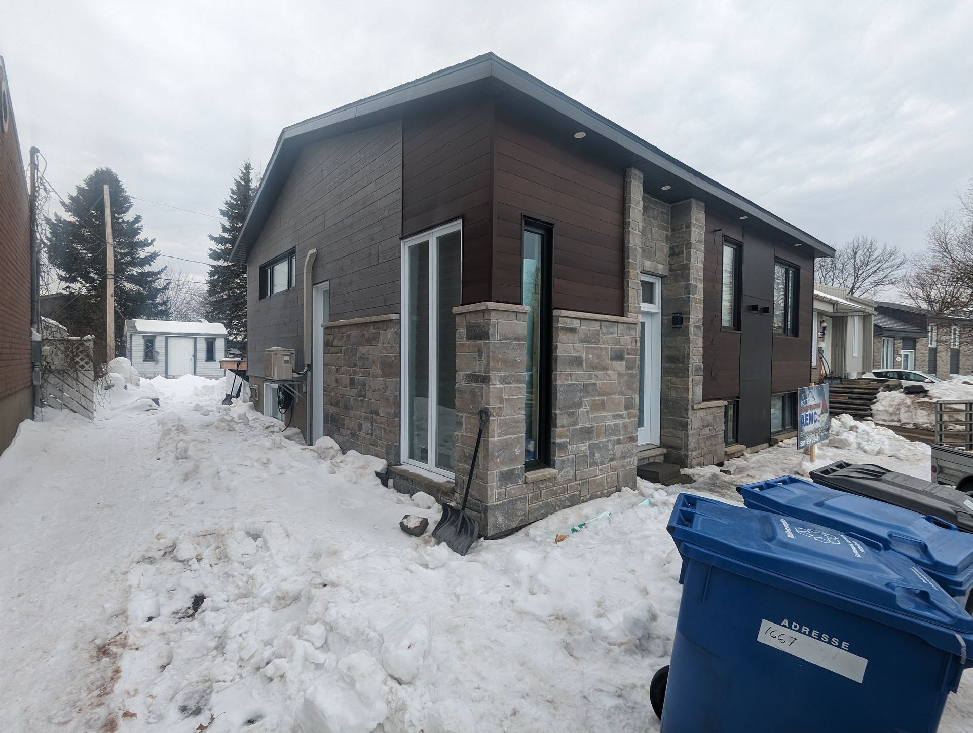 Une maison avec une poubelle bleue devant elle dans la neige.