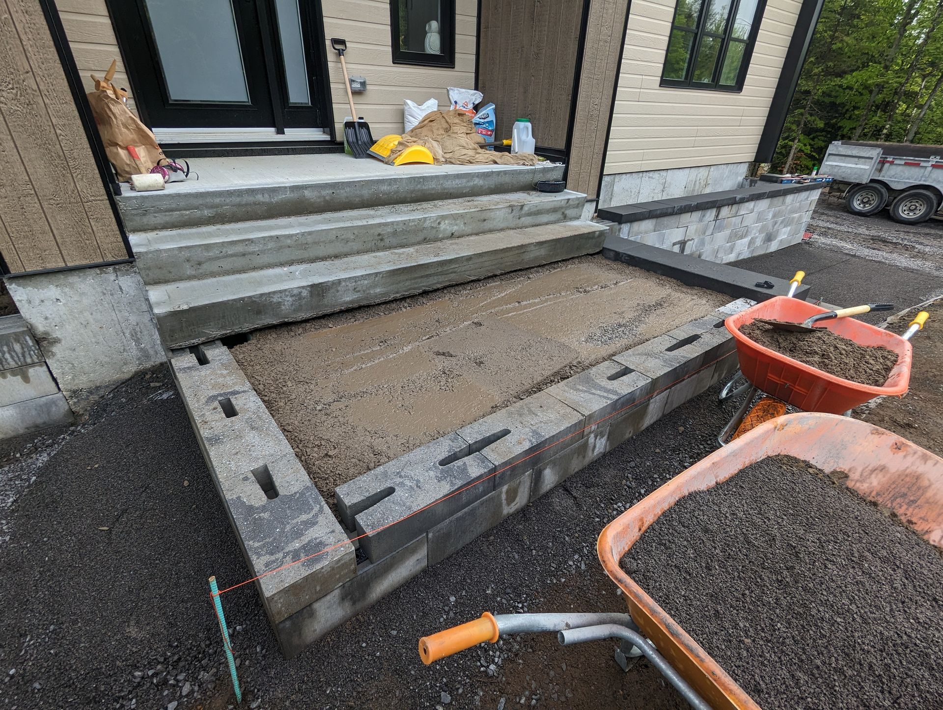 Une brouette remplie de terre est posée devant une maison en construction.