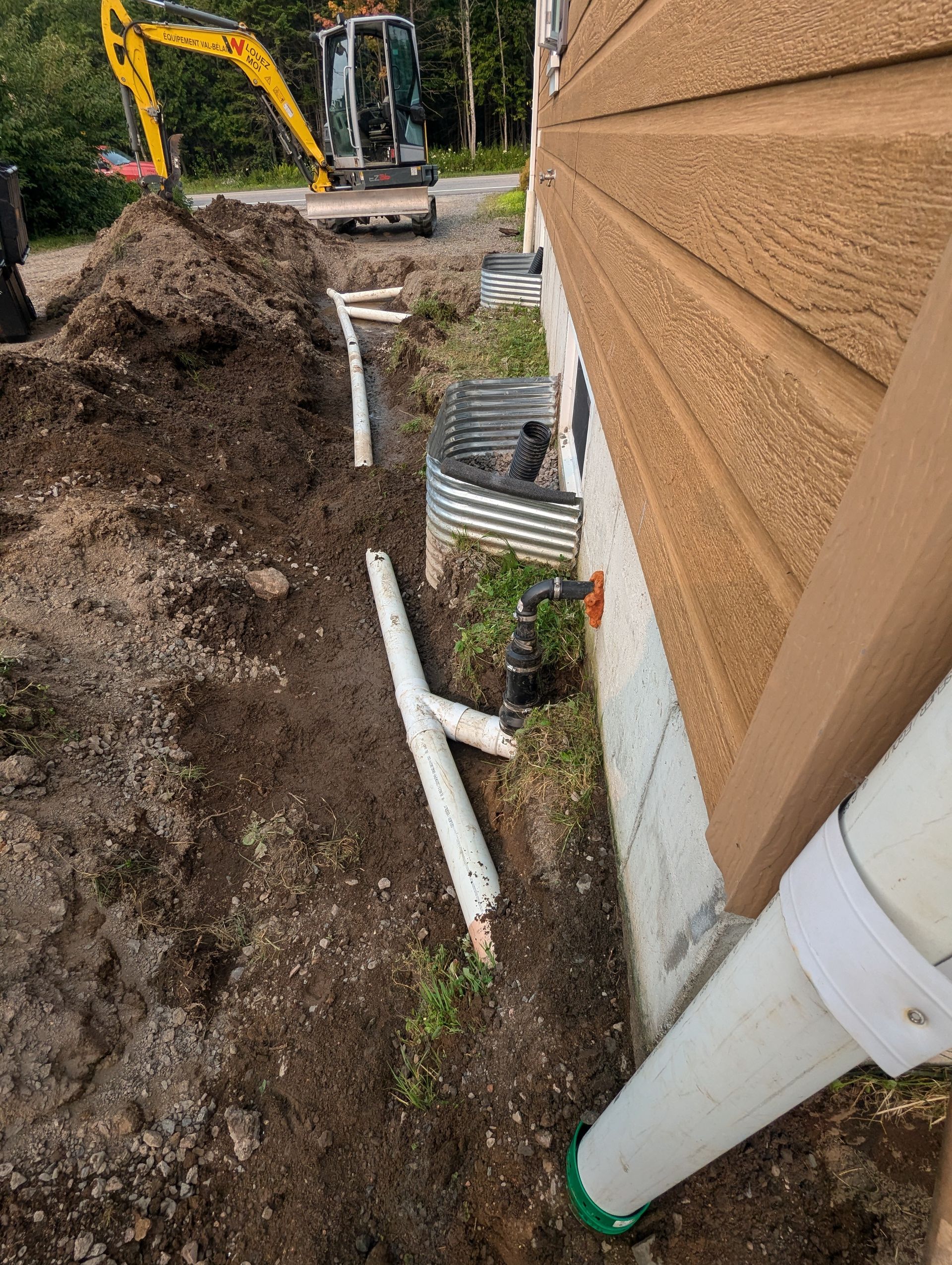 Une excavatrice jaune creuse un trou dans le sol à côté d'une maison.