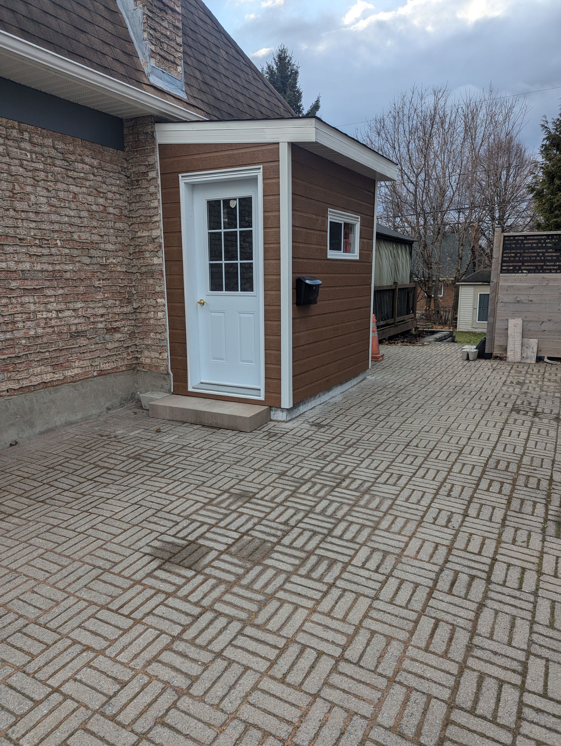 Un petit hangar en briques avec une porte blanche se trouve dans l'arrière-cour d'une maison.