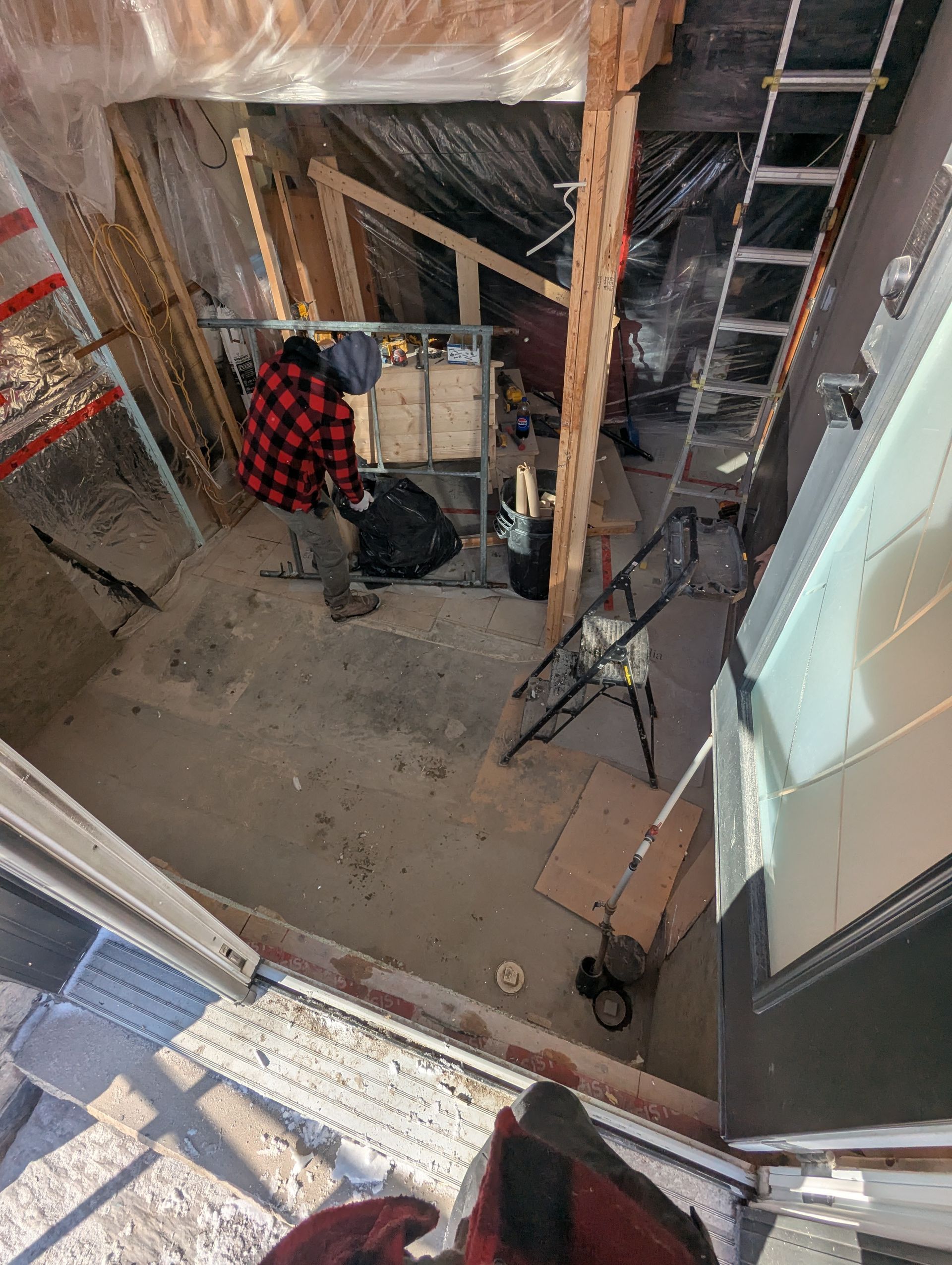 Un homme en chemise à carreaux se tient dans une pièce avec une échelle.