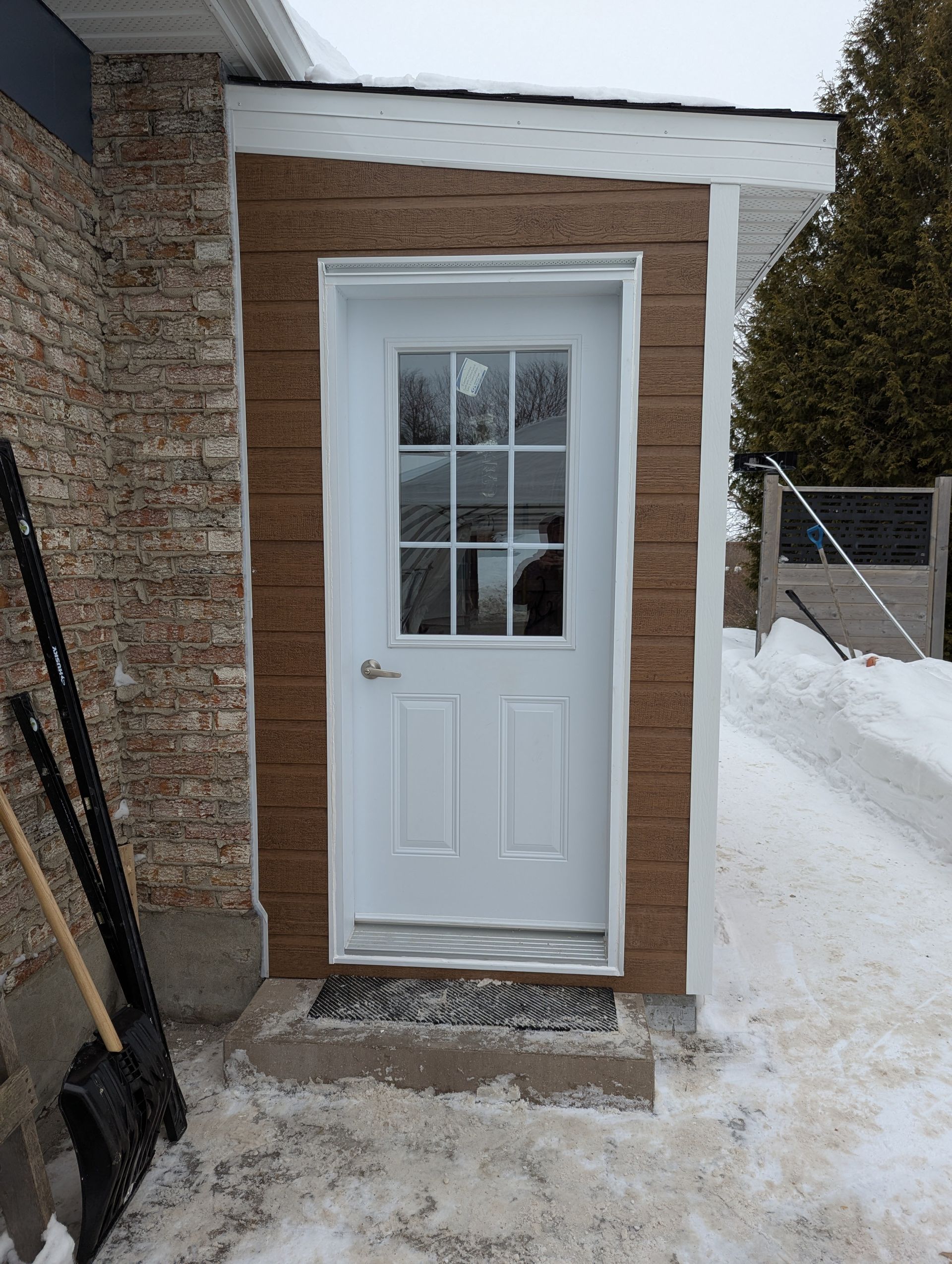 Une porte blanche avec une fenêtre est posée dans la neige à côté d'une pelle.