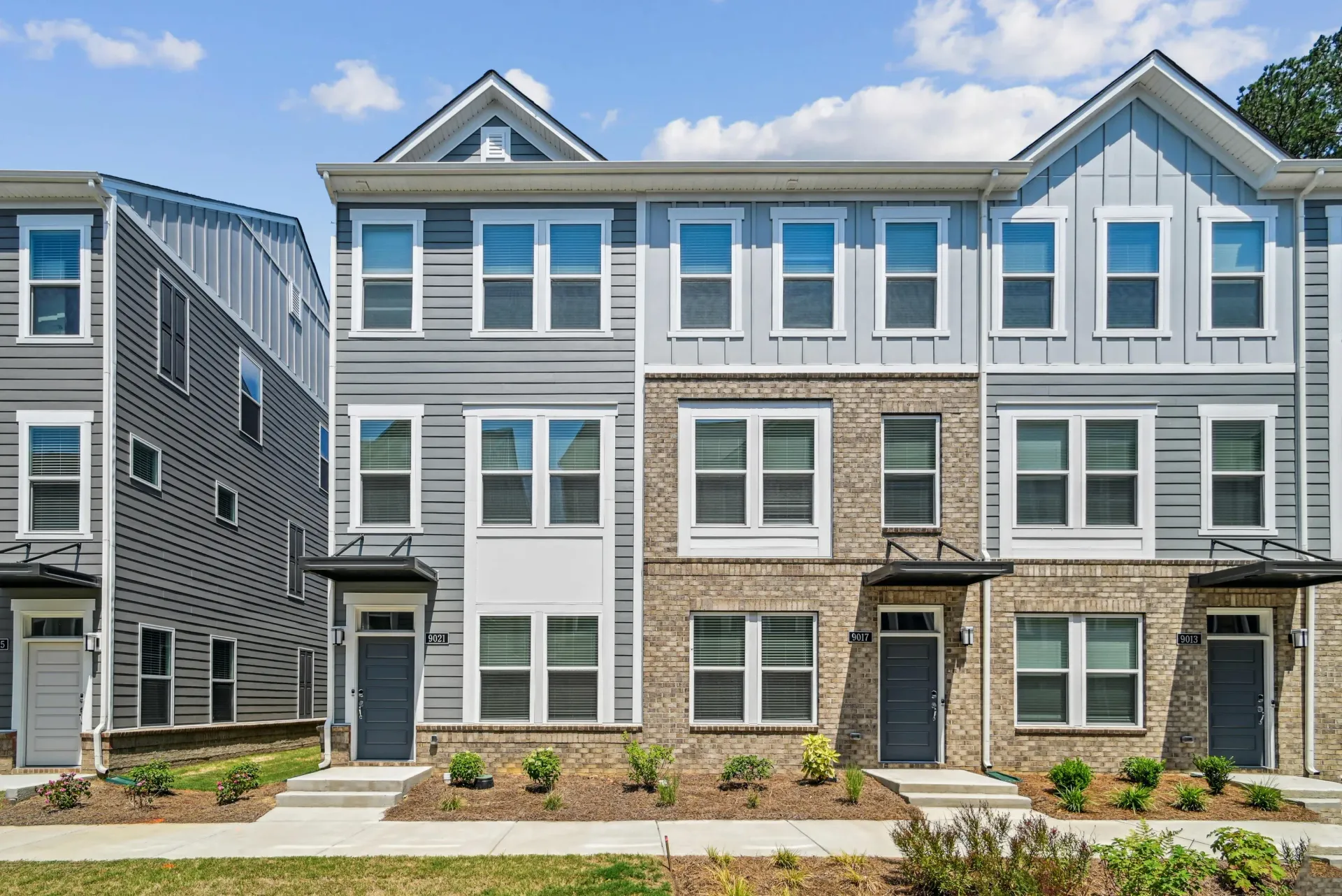 Row of modern townhomes with gray siding, brick accents, and front doors.