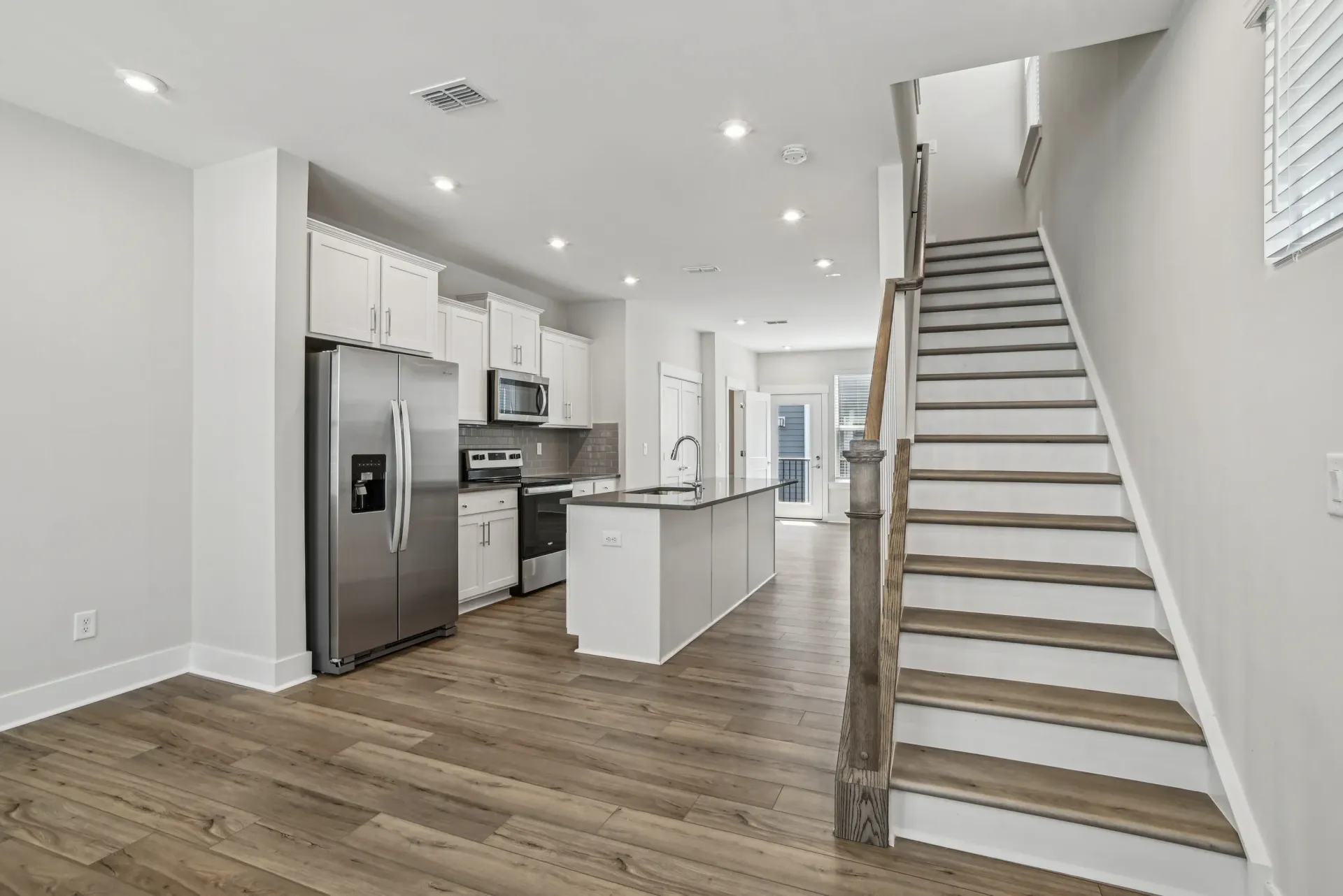 Open-concept kitchen in a modern apartment with island, stainless-steel appliances, and staircase.