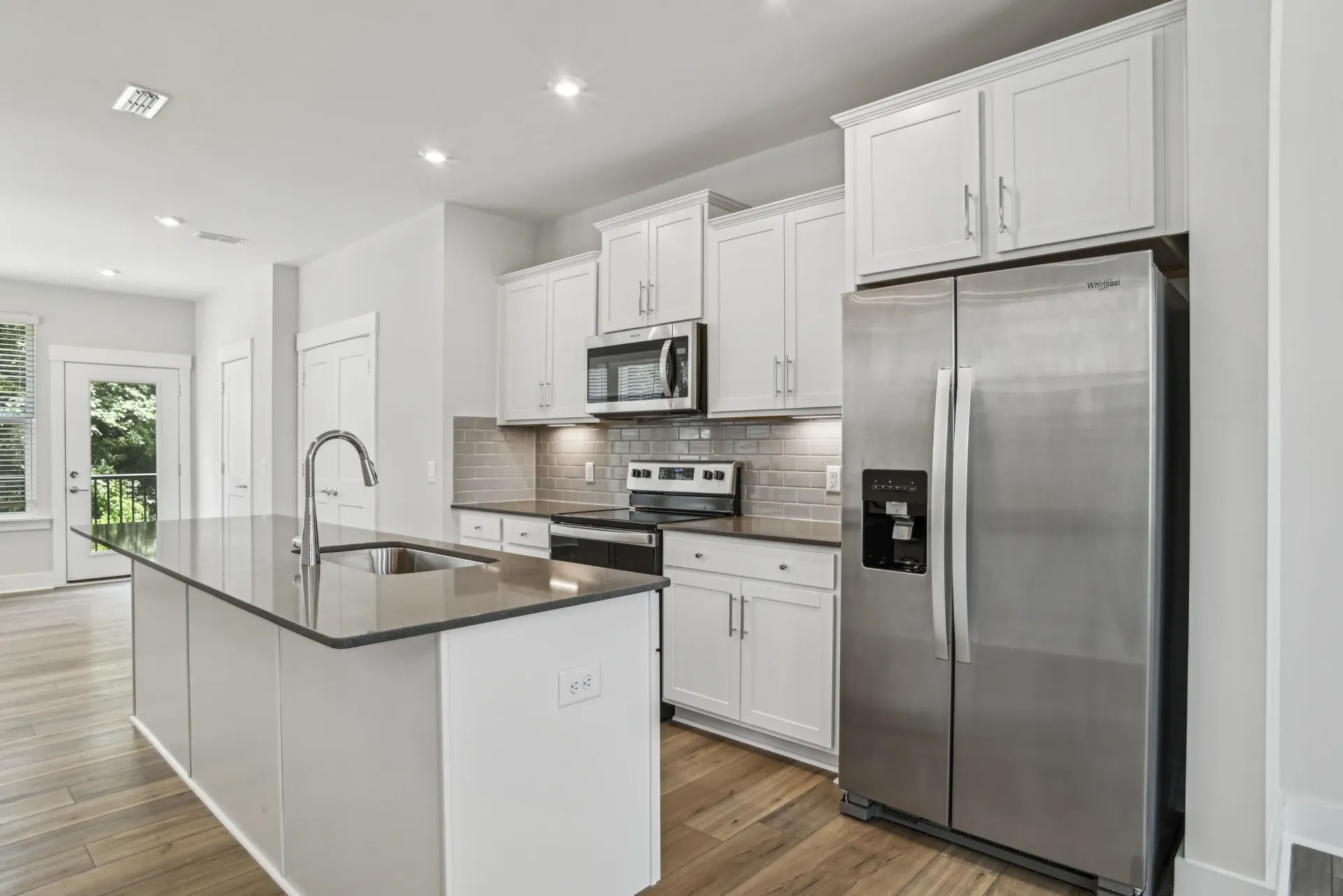 Bright white kitchen with an island, stainless steel fridge, and light wood flooring.
