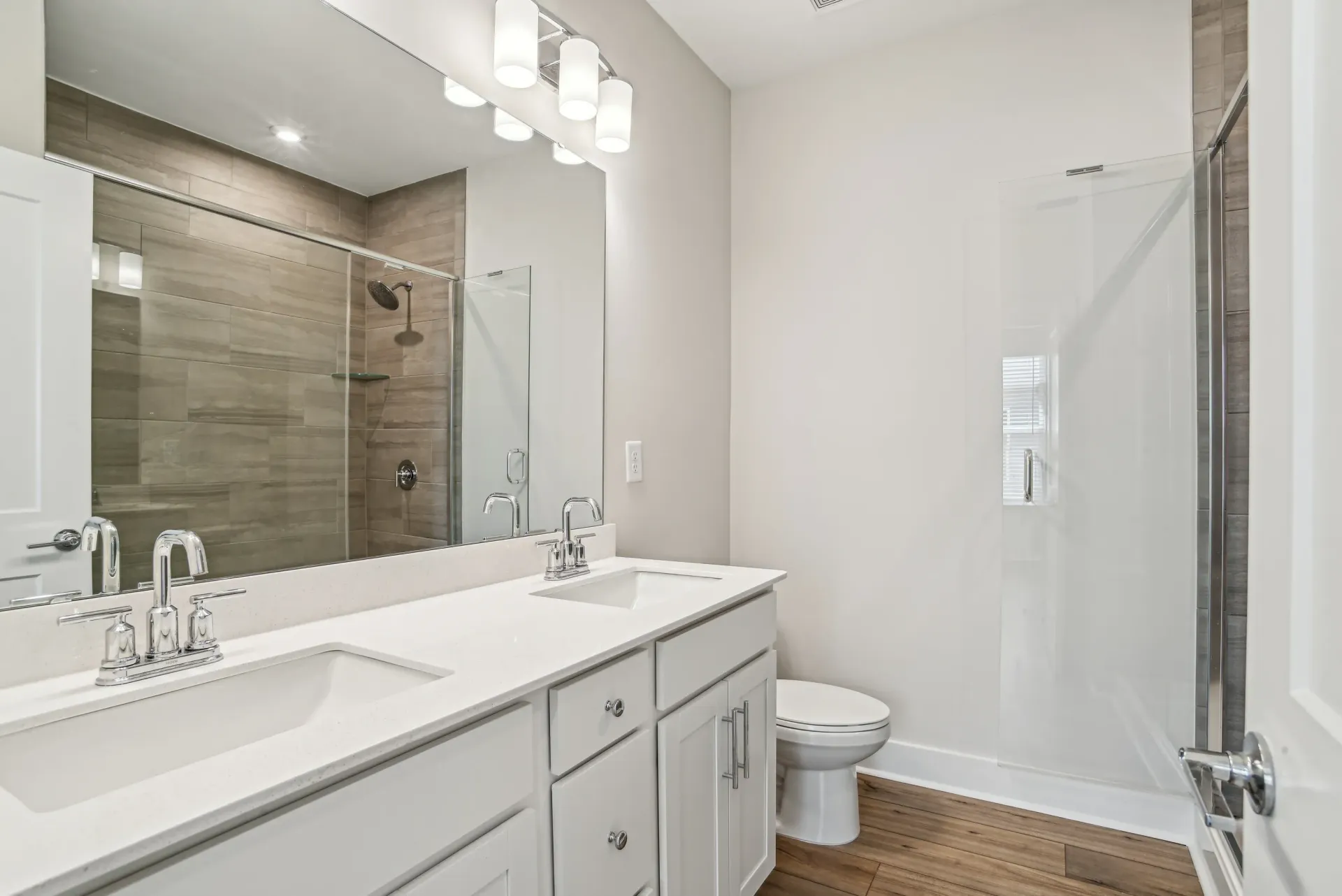 Two-sink bathroom vanity with large mirror and glass-enclosed shower in a modern apartment.