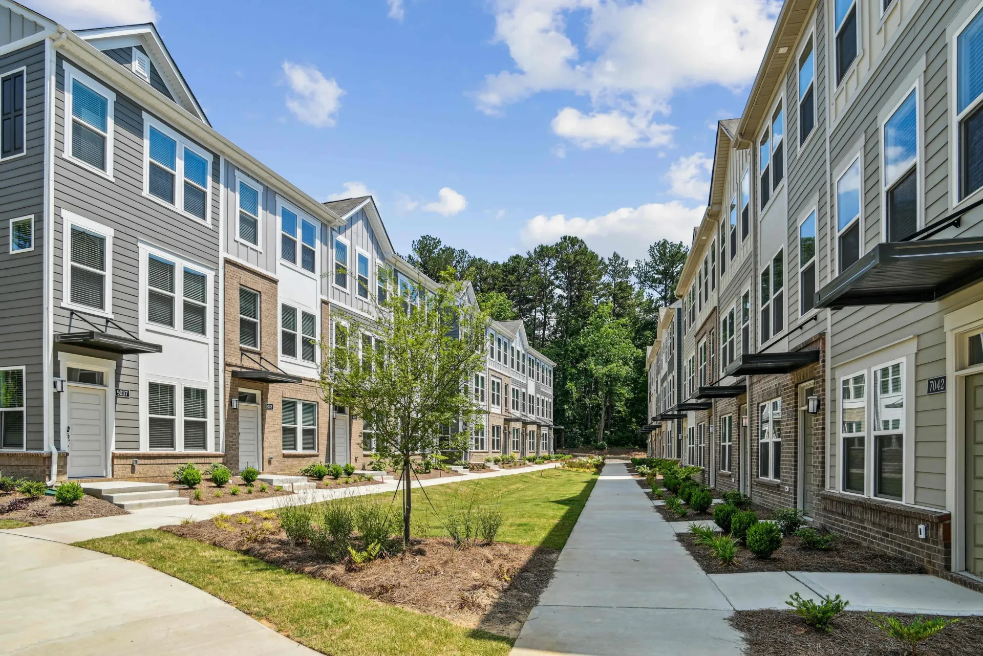 Exterior view of a modern apartment community with row townhome buildings, a central walkway, and landscaped grounds.