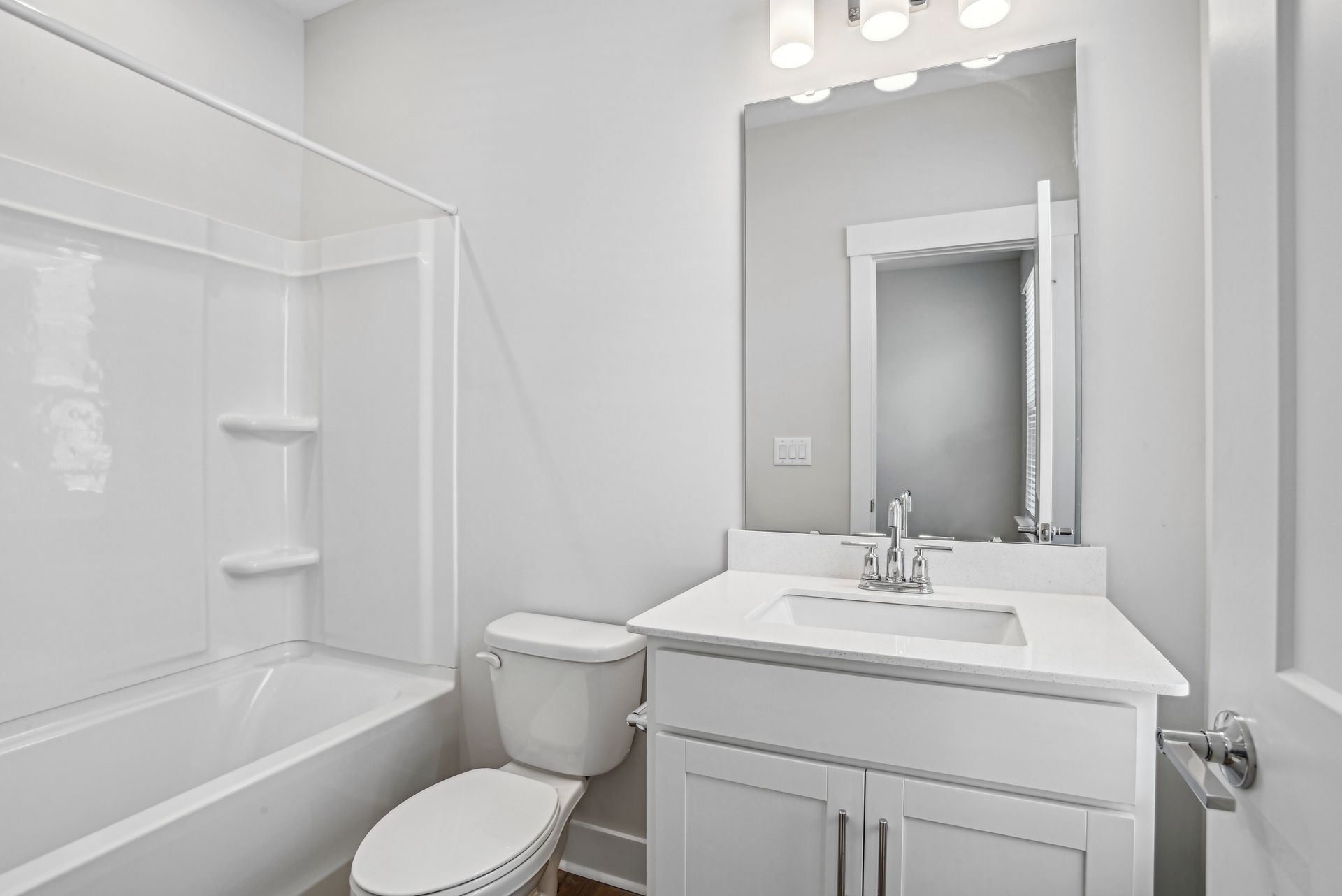 Bathroom with white fixtures: tub/shower, toilet, vanity with mirror and overhead lights.
