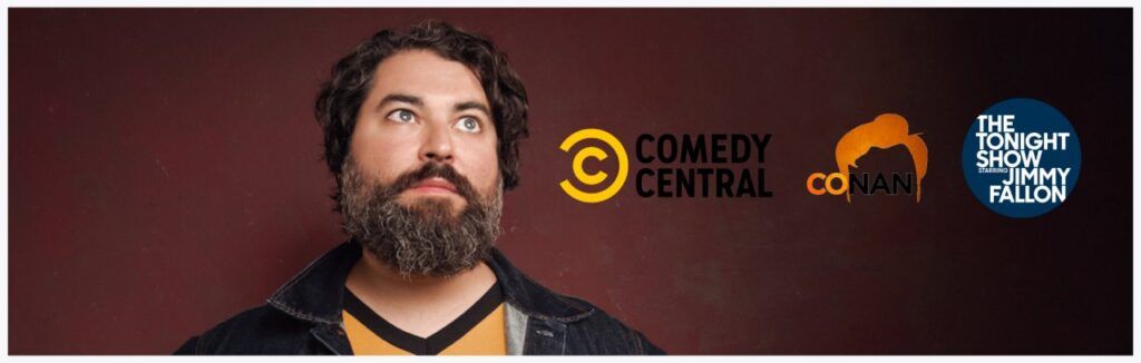 A man with a beard is standing in front of a comedy central logo