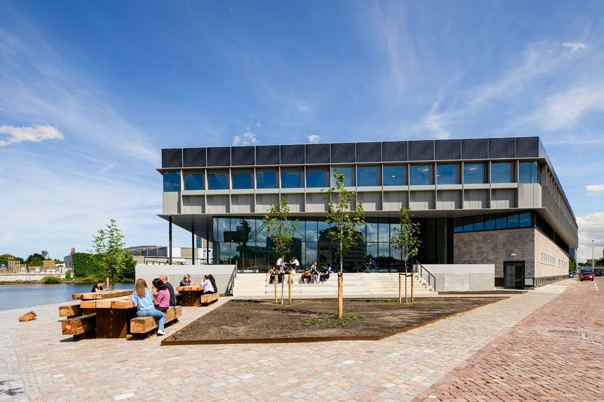 A group of people are sitting on benches in front of a large building.