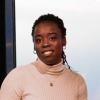 A woman wearing a turtleneck sweater and a necklace is smiling for the camera.