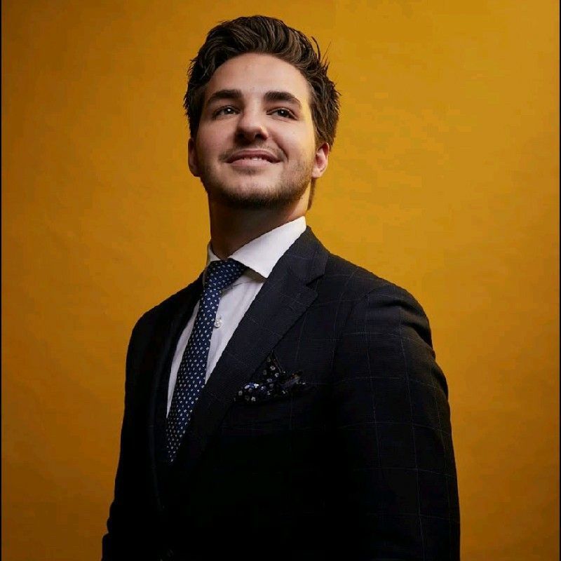 A man in a suit and tie is smiling in front of a yellow background.