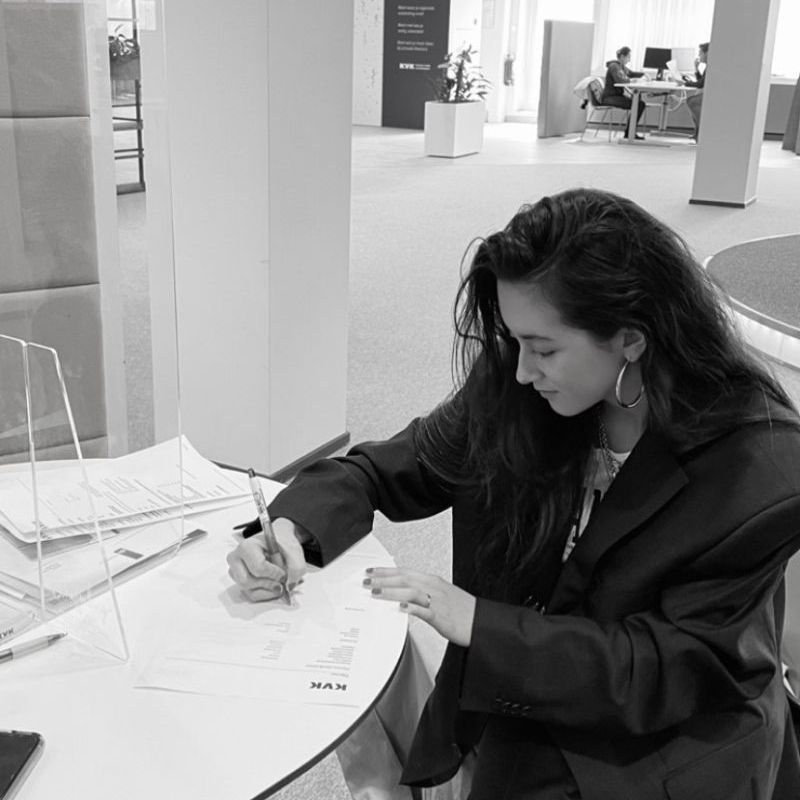 A woman is sitting at a table writing on a piece of paper
